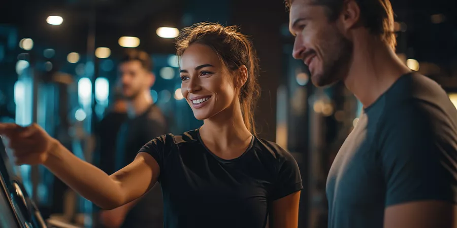 eine weibliche Fitnesstrainerin zeigt jemand anderen wie man ein Laufband bedient