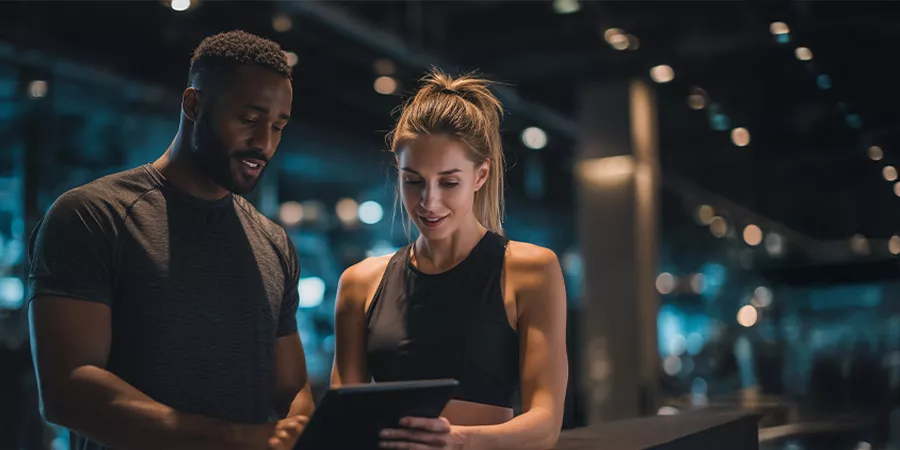 zwei sportliche Personen stehen beinander in einem Fitnessstudio und schauen sich etwas auf einem Tablet an