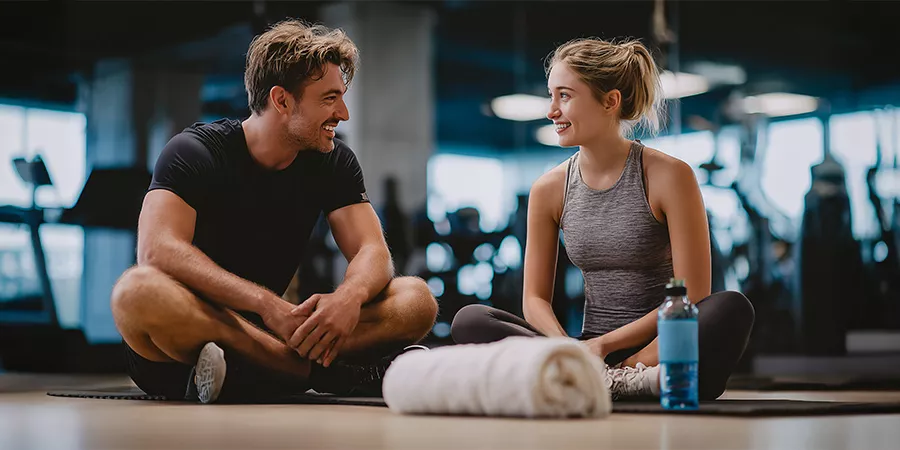 zwei sportliche Leute sitzen auf dem Boden eines Fitnessstudios und unterhalten sich
